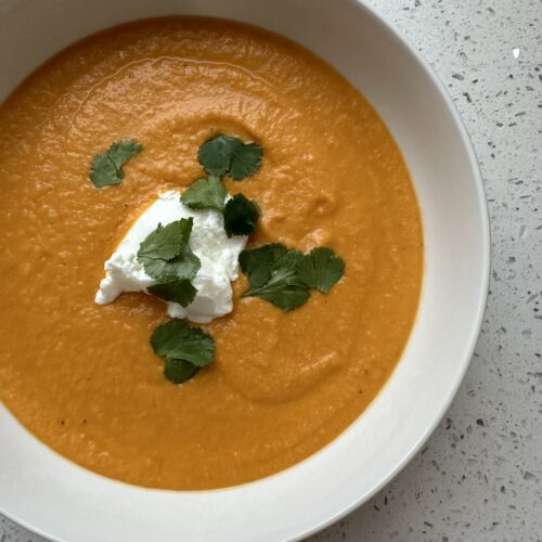 A bowl of carrot ginger soup topped with greek yogurt, cilantro, and hemp hearts