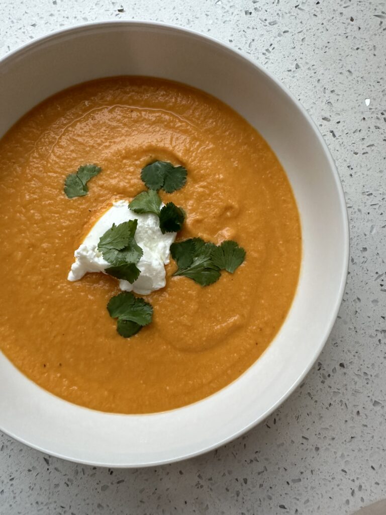 A bowl of carrot ginger soup topped with greek yogurt, cilantro, and hemp hearts